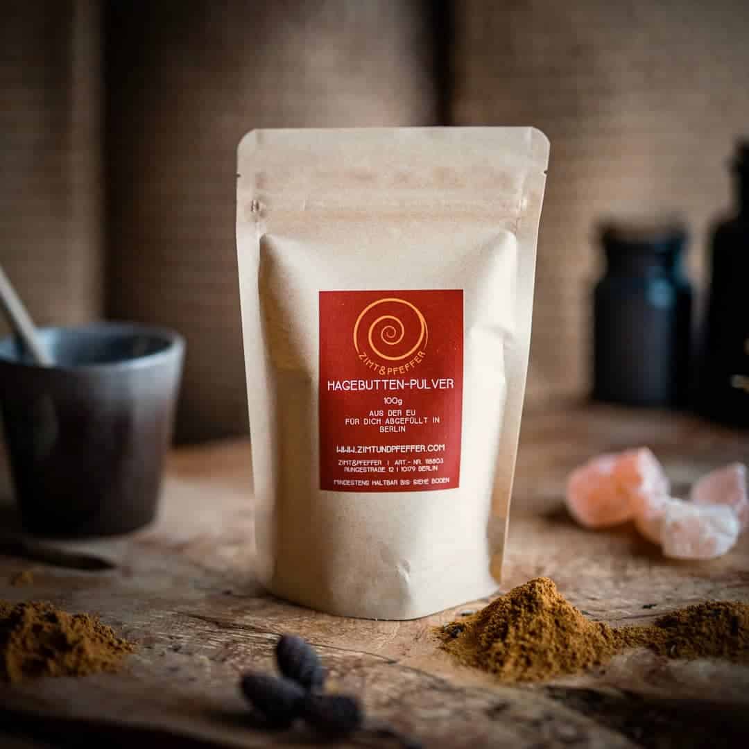 Ein Eine Zip-Tüte auf einem Olivenholzbrett. Bei dem Produkt handelt es sich um Hagebutte, mit einer Füllmenge von 100g.
