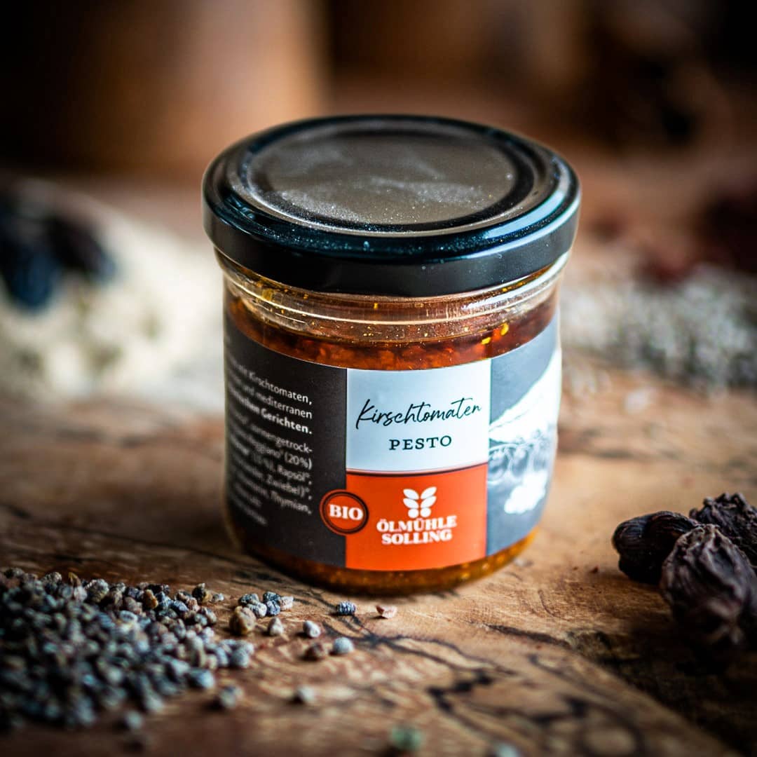 Ein Glas Kirschtomaten Pesto auf einem Olivenholzbrett.