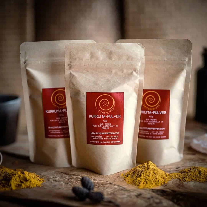 Drei 100g Tüten Kurkuma Pulver auf einem Olivenholzbrett