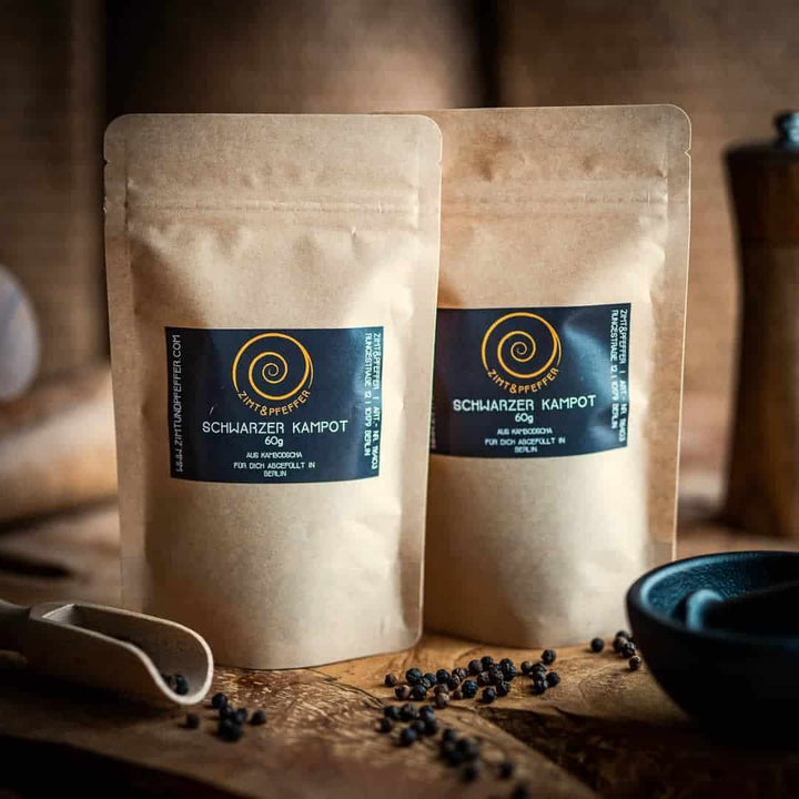 Schwarzer Kampot Pfeffer in zwei nachhaltigen Kraftpapiertüten auf einem Olivenholzbrett von Zimt&Pfeffer