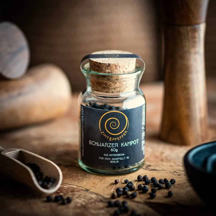 Schwarzer Kampot Pfeffer in einem Glas mit Presskorken auf einem Olivenholzbrett von Zimt&Pfeffer