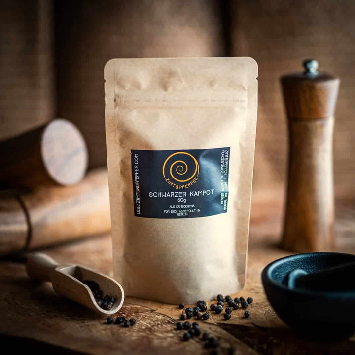 Schwarzer Kampot Pfeffer in einer nachhaltigen Kraftpapiertüte auf einem Olivenholzbrett von Zimt&Pfeffer