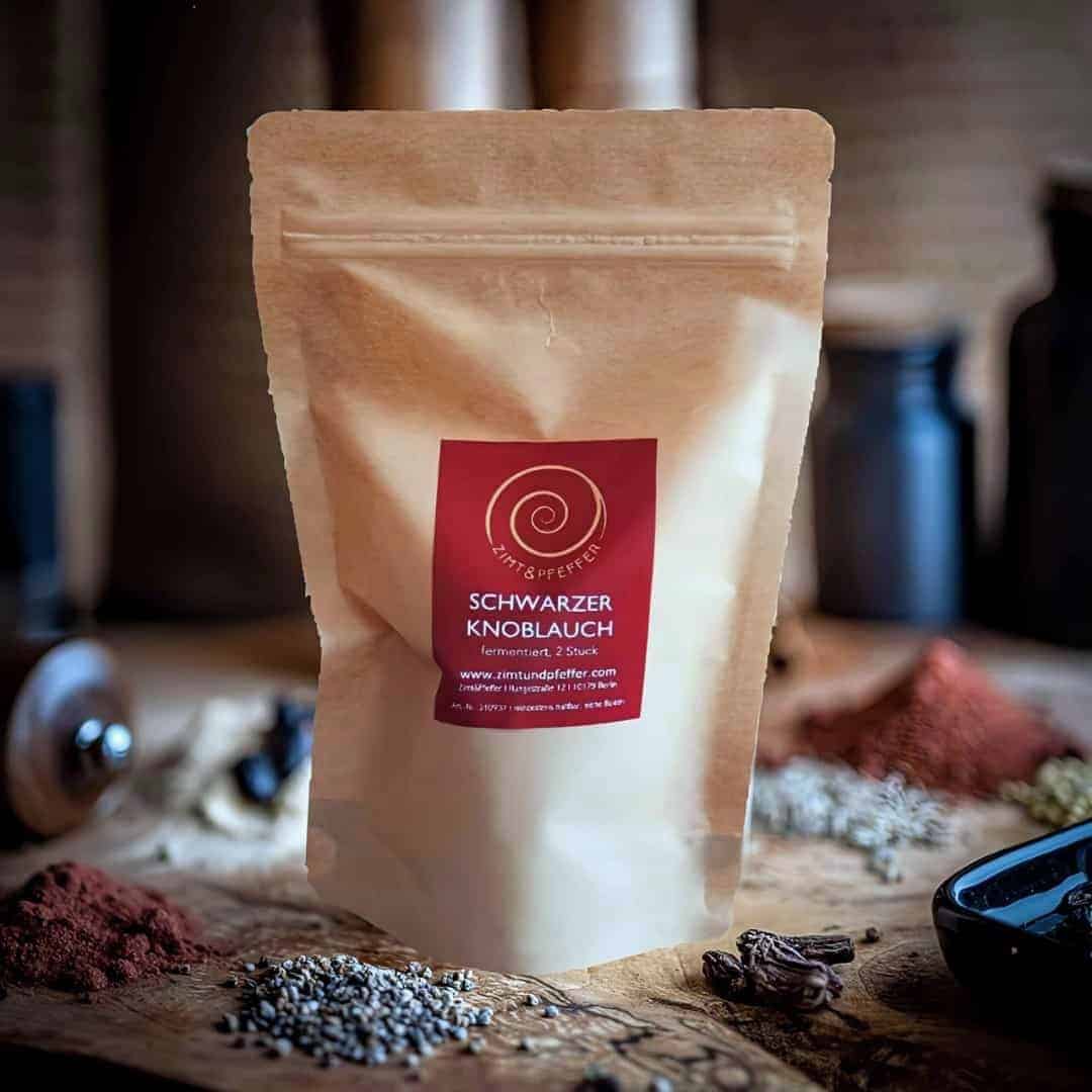 Eine Tüte mit 2 Knollen Schwarzer Knoblauch auf einem Olivenholzbrett.