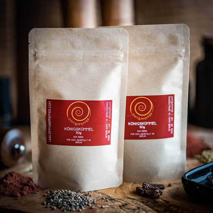 Zwei Tüten mit jeweils mit 50g Königskümmel auch Ajowan genannt auf einem Olivenholzbrett.