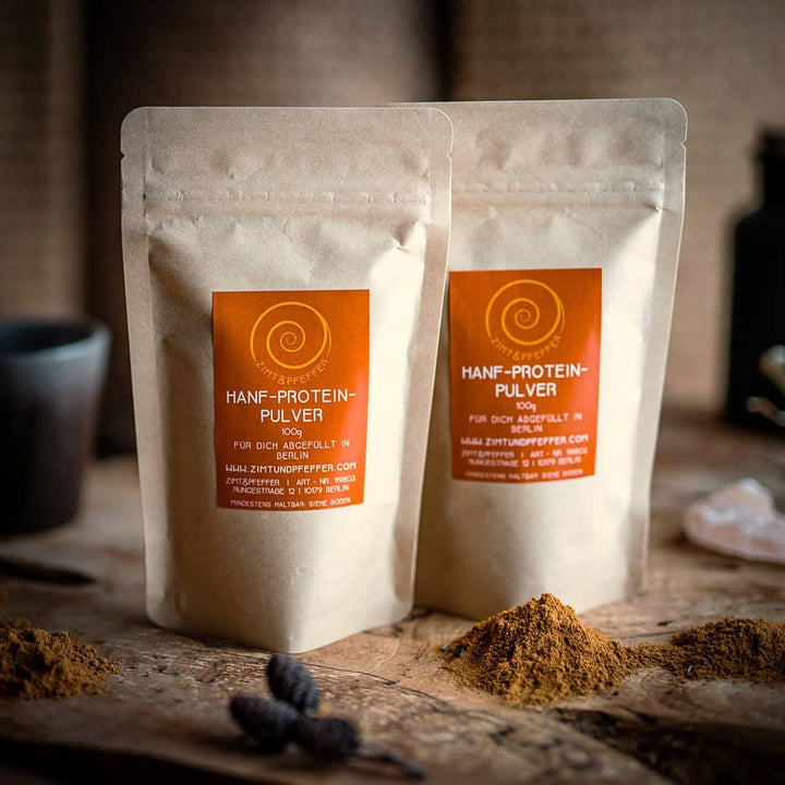 Zwei Zip-Tüten auf einem Olivenholzbrett. Bei dem Produkt handelt es sich um Hanf-Proteinpulver, mit einer Füllmenge von 100g.
