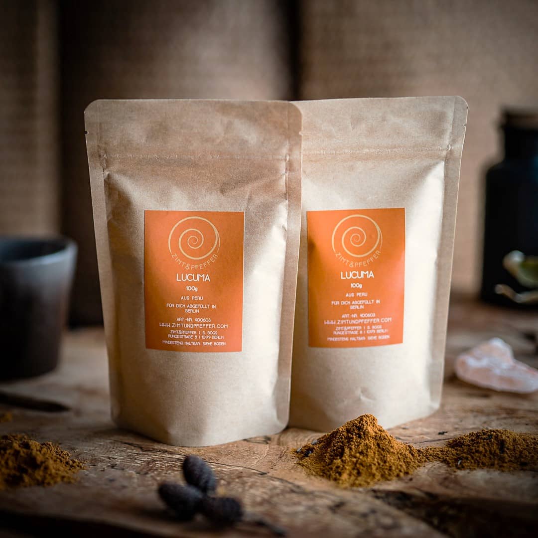 Drei Zip-Tüten aus Kraftpapier auf einem Olivenholzbrett. Bei dem Produkt handelt es sich um Lucuma, mit einer Füllmenge von 100g.