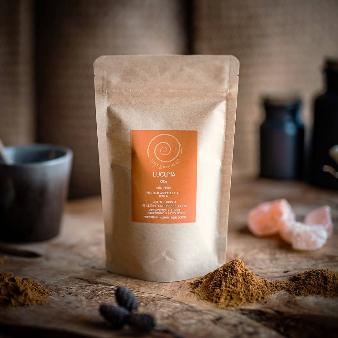 Eine Zip-Tüte aus Kraftpapier auf einem Olivenholzbrett. Bei dem Produkt handelt es sich um Lucuma, mit einer Füllmenge von 100g.