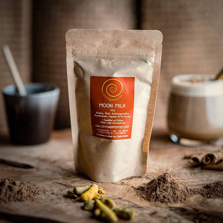 Ein  Nachfüllpack Moon Milk 100g auf einem Olivenholzbrett. Bei dem Produkt handelt es sich um die Mischung Moon Milk, aus purem Rohkakao, Zimt, Ashwagandha, Kardamom, Ingwer und Kurkuma.