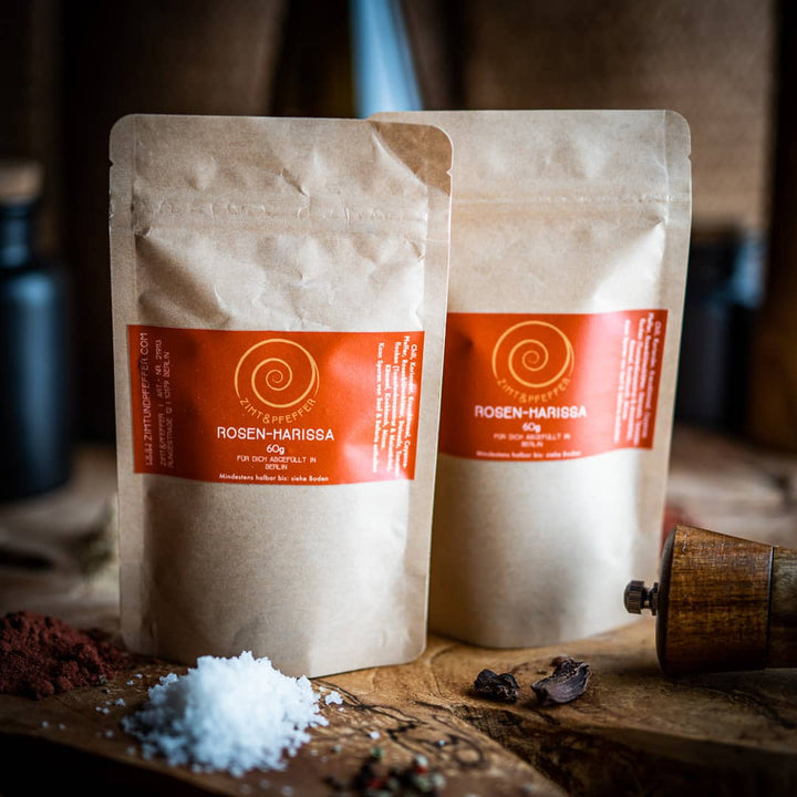 Zwei 60g Tüten Rosen-Harissa auf einem Olivenholzbrett.