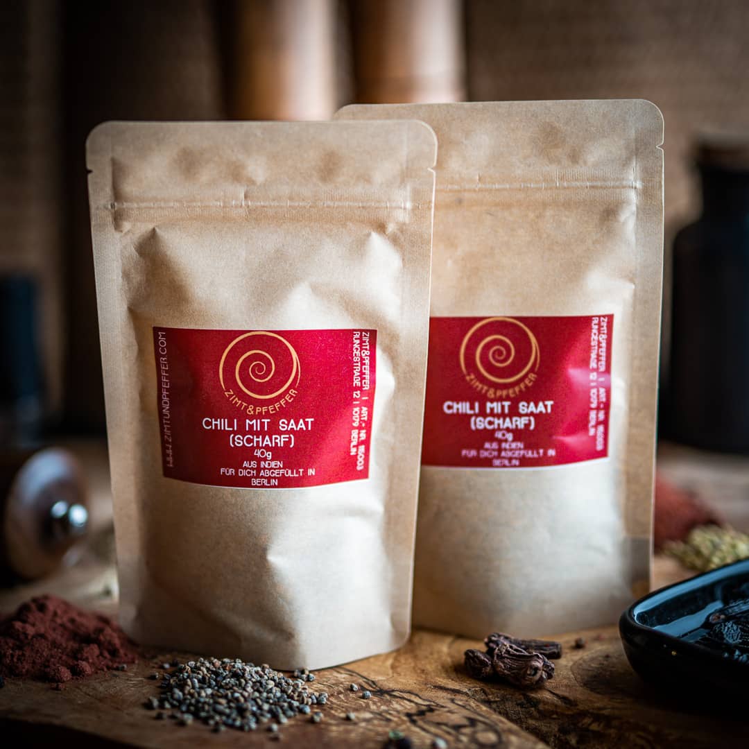 Zwei Tüten Chili Flocken (scharf) auf einem Olivenholzbrett.