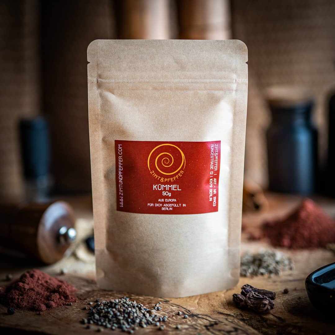 Eine 50g Tüte Kümmel auf einem Olivenholzbrett.