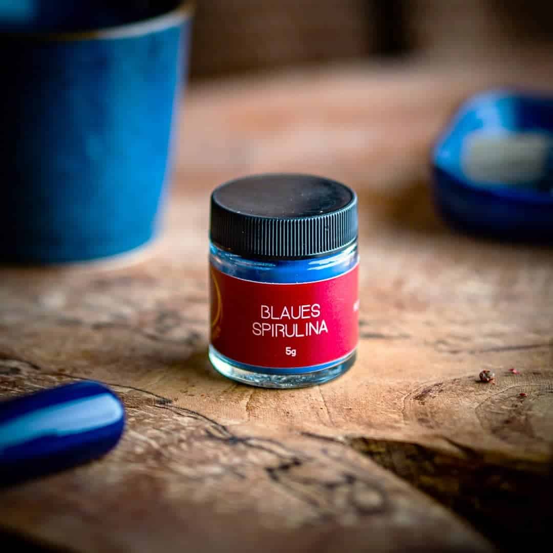 Ein kleines Glas mit Drehverschluss auf einem Olivenholzbrett. Bei dem Produkt handelt es sich um Blaues Spirulina, mit einer Füllmenge von 5g.