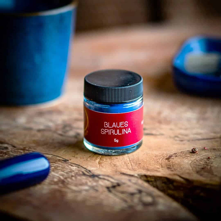 Blaues Spirulina 5 g im kleinen Glas mit Drehverschluss auf einem Olivenholzbrett