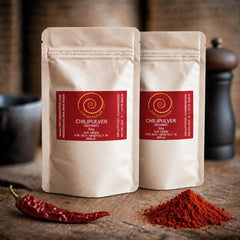 Eine Tueten mit je 50 g Chili Pulver auf einem Olivenholzbrett