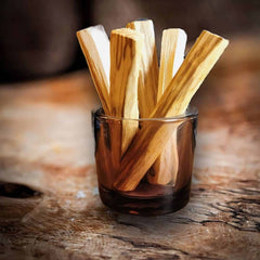 Fünf Palo Santo Sticks in einem Glas auf einem Olivenholzbrett.