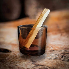 Ein Palo Santo Stick in einem Glas auf einem Olivenholzbrett.