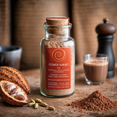 Ein 100g Glas Power Kakao auf einem Olivenholzbrett. Eine Mischung aus Rohkakao, Maca, Kardamom und Lucuma.
