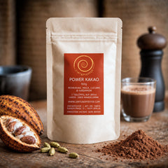 Eine 100g Tüte Power Kakao auf einem Olivenholzbrett. Eine Mischung aus Rohkakao, Maca, Kardamom und Lucuma.
