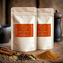 Zwei Nachfüllpacks Ras el Hanout stehen auf einem Olivenholzbrett. Die nordafrikanische Mischung besteht aus Kurkuma, Koriander, Fenchel, Zimt, Pfeffer, Ingwer, Piment, Cumin, Chili, Kardamom, Bockshornkleesaat, Muskatnuss und Anis und hat eine Füllmenge von 60 g.