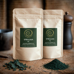 Spirulina Pulver von Zimt&amp;Pfeffer in 
zwei 80 g Tüten Spirulina Pulver auf einem Olivenholzbrett 
