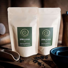 Spirulina Pulver von Zimt&amp;Pfeffer in 
zwei 80 g Tüten Spirulina Pulver auf einem Olivenholzbrett 