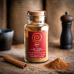 Zimt aus Vietnam, ein 100 g Glas auf einem Olivenholzbrett. Dieser Zimt ist aromatisch, würzig, süß und leicht scharf zugleich.