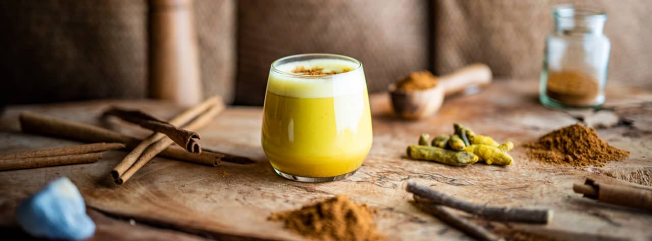 Ein Glas Goldene Milch auf einem Olivenholzbrett – Superfood Lattes kaufen