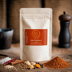 Eine 50 g Tüte Ghati Masala auf einem Olivenholzbrett.