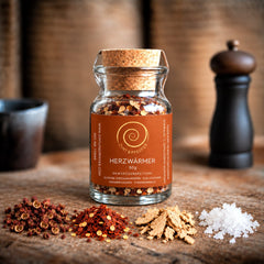 Ein Glas Herzwärmer mit 50 g auf einem Olivenholzbrett. Eine harmonisch abgestimmte Gewürzzubereitung aus Szechuan Pfeffer, Chili- und Ingwerflocken sowie feinstem Pyramidensalz.