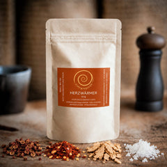 Eine Tüte Herzwärmer mit 50 g auf einem Olivenholzbrett. Eine harmonisch abgestimmte Gewürzzubereitung aus Szechuan Pfeffer, Chili- und Ingwerflocken sowie feinstem Pyramidensalz.