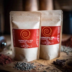 Zwei 50g Tueten Paprika geräuchert scharf auf einem Olivenholzbrett.