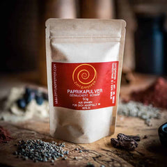 Eine 50g Tuete Paprika geräuchert scharf auf einem Olivenholzbrett.