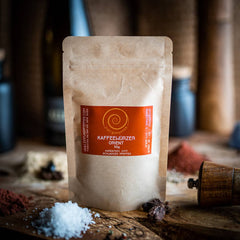 Eine 50g Tüte Kaffeewürzer Orient auf einem Olivenholzbrett.