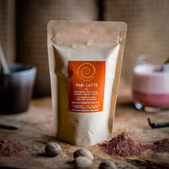 Eine 100g Tüte Pink Latte auf einem Olivenholzbrett.