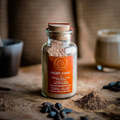 Ein 100g Glas Power Kakao auf einem Olivenholzbrett. Eine Mischung aus Rohkakao, Maca, Kardamom und Lucuma.