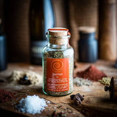 Ein 60g Glas Zahtar auf einem Olivenholzbrett. Eine Gewürzmischung aus Sesamsaat, Zumaq (Sumachfrüchte gemahlen), Thymian und Oregano.