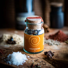 Ein Glas Herzwärmer mit 50g auf einem Olivenholzbrett. Eine harmonisch abgestimmte Gewürzzubereitung aus Szechuan Pfeffer, Chili- und Ingwerflocken sowie feinstem Pyramidensalz.