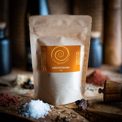 Eine Tüte Herzwärmer mit 50g auf einem Olivenholzbrett. Eine harmonisch abgestimmte Gewürzzubereitung aus Szechuan Pfeffer, Chili- und Ingwerflocken sowie feinstem Pyramidensalz.