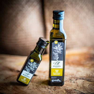 Zwei Flaschen BIO Mandelöl 100ml und 250 ml, produziert von der Ölmühle Solling stehen auf einem Olivenholzbrett.