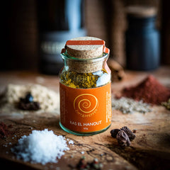 Ein Glas Ras el Hanout steht auf einem Olivenholzbrett. Die nordafrikanische Mischung besteht aus Kurkuma, Koriander, Fenchel, Zimt, Pfeffer, Ingwer, Piment, Cumin, Chili, Kardamom, Bockshornkleesaat, Muskatnuss und Anis und hat eine Füllmenge von 60g.