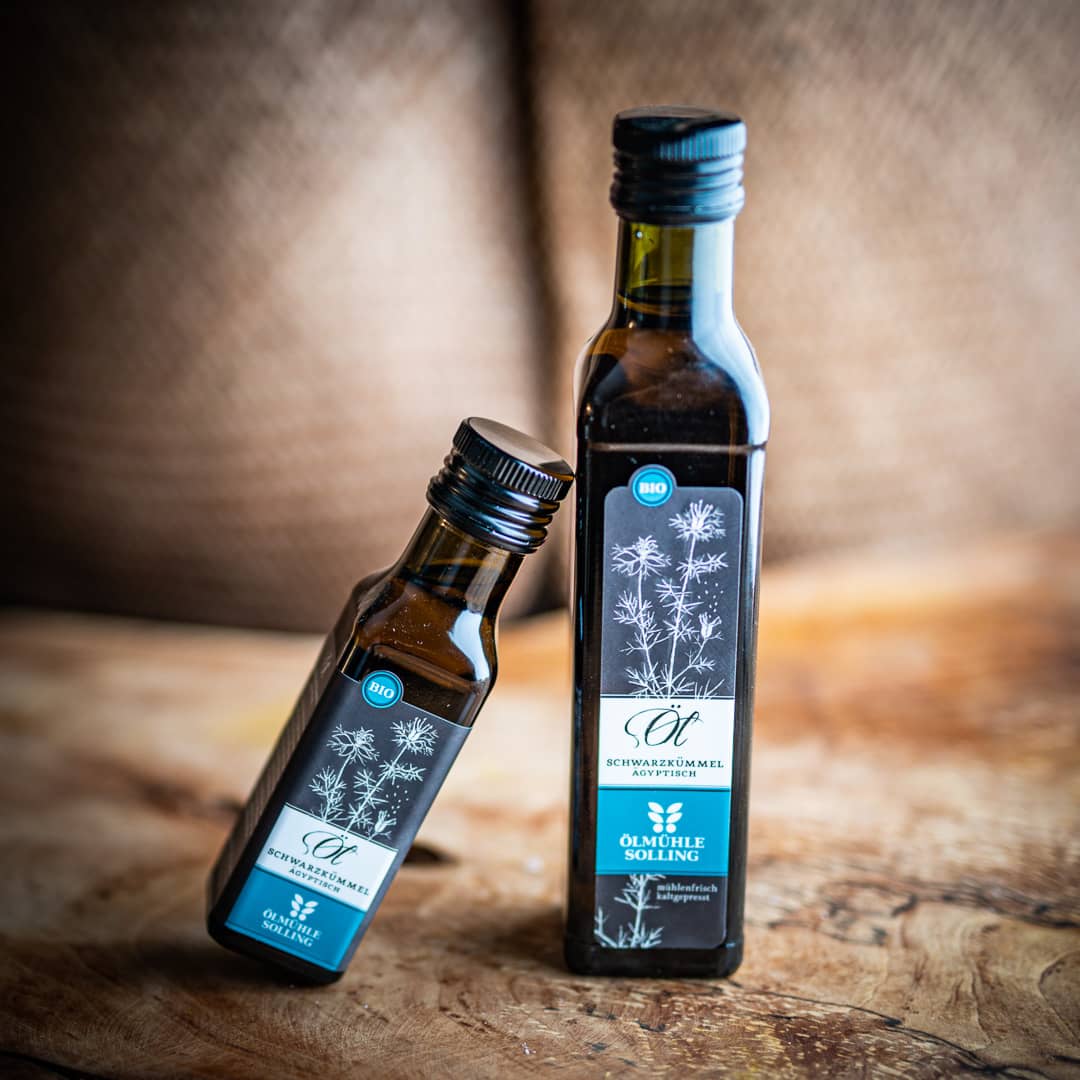 Zwei Flaschen mit Ägyptisches Schwarzkümmelöl, 100ml und 250ml, produziert von der Ölmühle Solling stehen auf einem Olivenholzbrett.