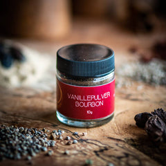 Bourbon Vanille Pulver aus Madagaskar – 100 % natürlich. Ein 10 g Glas Bourbon Vanille Pulver auf einem Olivenholzbrett.